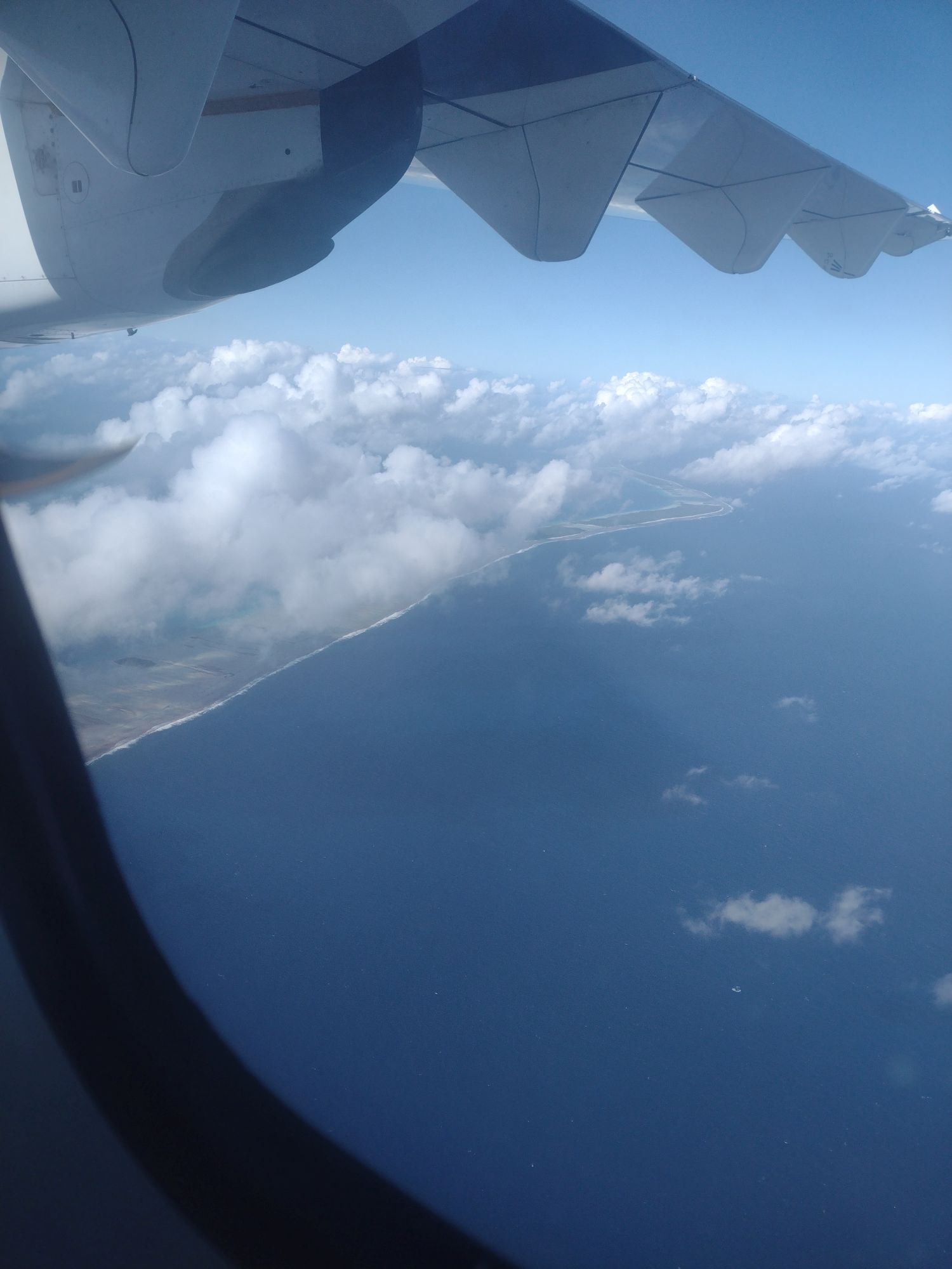 Foto aus Flugzeug mit Sicht auf Wolken und Atoll